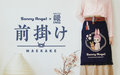 White background with navy blue text "Sonny Angel and Anything" collaboration "Maekake" apron. Below text is a paper lantern, cherry blossom plant, and person. Person is wearing a pink shirt, tan skirt and navy blue apron. Apron has red and white striped ties, navy fringe, wrapped around the waist of the figure. Red and white striped pocket holds Rabbit Sonny Angel minifigure. Apron design: Rabbit Sonny Angel beside Robby encircled with cherry blossoms, and text: "Sonny Angel" "He may bring you happiness?!"